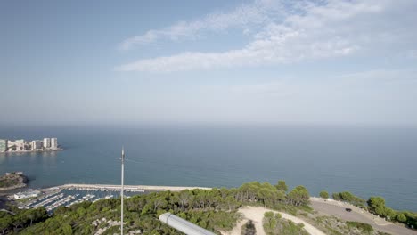 Close-up-4K-discover-vertical-drone-view-next-to-a-spinning-marine-radar-on-top-of-a-hill-in-Oropesa-del-Mar,-facing-the-blue-Mediterranean-Sea,-Spain