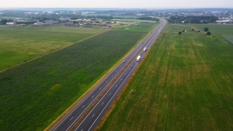 Aerial-shot-of-the-traffic-on-the-road-between-the-green-cultivated-fields-in-the-evening-in-Lithuania