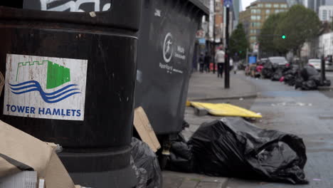 A-man-on-an-electric-scooter-passes-black-bin-bags-and-rubbish-piled-up-around-a-refuse-bin-on-the-Whitechapel-Road-following-two-weeks-of-refuse-strikes-in-Tower-Hamlets-Borough