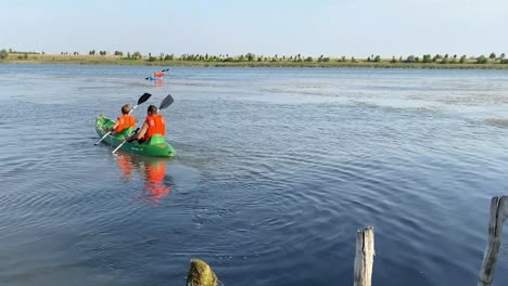 Back-view-of-pair-in-orange-lifejackets-kayaking-on-lake-in-wildlife