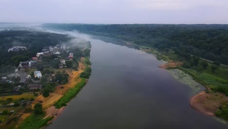 drone-shot-of-a-wide-Nemunas-river-with-a-green-forest-and-houses-on-the-bank-on-a-cloudy-day