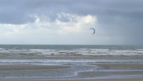 Einsamer-Kitesurfer-Beim-Kitesurfen-Auf-Stürmischer-See,-Kamerafahrt-Vom-Strand-Aus
