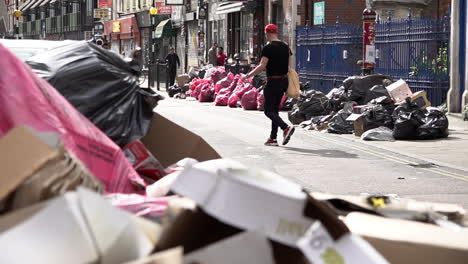 In-slow-motion-a-man-walks-past-mounds-of-rubbish-sand-black-bin-bags-on-the-Whitechapel-Road-following-two-weeks-of-refuse-strikes-in-Tower-Hamlets-Borough