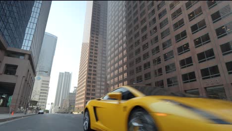 Yellow-Sports-Car-Driving-Under-Tall-Buildings-of-Downtown-Los-Angeles,-California