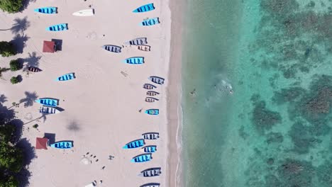 Top-down-aerial-view-of-exotic-sand-beach-with-stranded-small-boats-and-swimmers