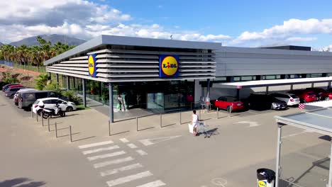 Static-view-Lidl-grocery-store,-people-entering-and-exiting-the-building,-sunny-blue-sky-day