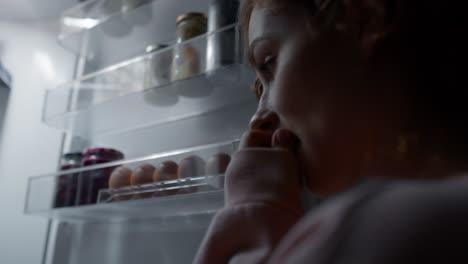 Undecided-young-caucasian-woman-checking-fridge-for-some-food-at-night.