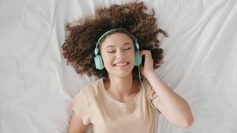 Young-woman-lying-on-the-bed-and-listening-to-music