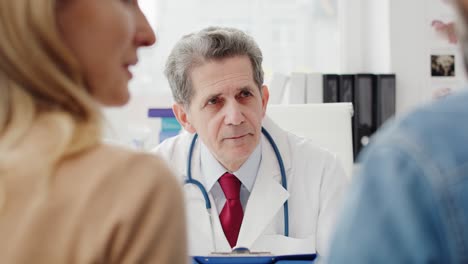 Handheld-view-of-couple-talking-with-doctor-in-doctor's-office
