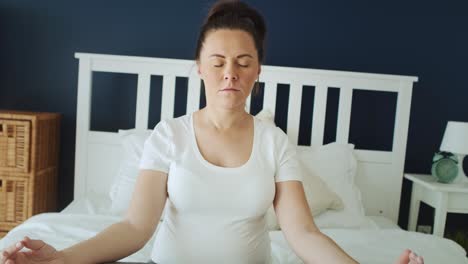 Zoom-out-video-of-pregnant-woman-meditating-in-bed.