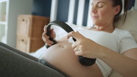 Tracking-video-of-pregnant-woman-putting-headphones-on-pregnant-abdomen.