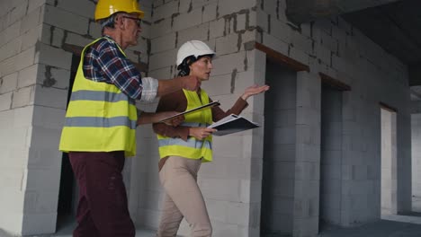 Male-and-female-caucasian-engineers-talking-while-walking-up-on-stairs-on-the-construction-site.