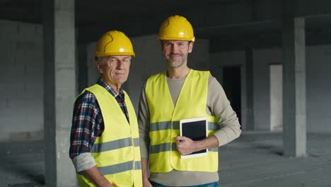 Portrait-of-two-caucasian-engineers-holding-digital-tablet-while-standing-on-construction-site.