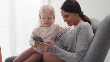 Caucasian-woman-in-advanced-pregnancy-and-her-elementary-aged-daughter-using-mobile-phone-at-home.