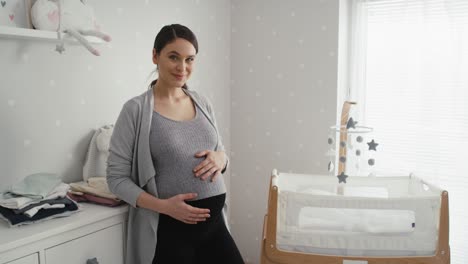Thoughtful-caucasian-woman-in-advanced-pregnancy-standing-in-the-baby's-room-next-to-the-crib.
