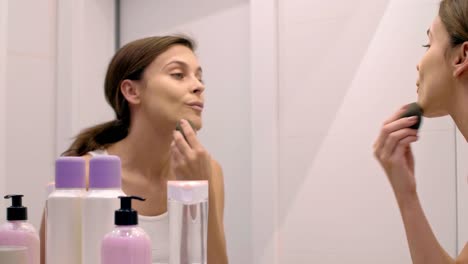 Woman-applying-beauty-product-on-her-face-in-bathroom