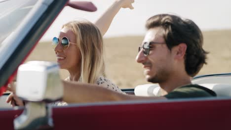 Side-view-of-smiling-couple-driving-in-a-cabriolet