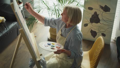 Top-view-of-senior-female-artist-painting-at-home