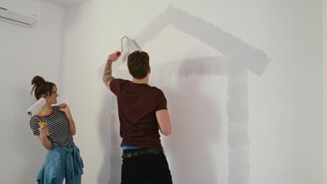 Young-caucasian-couple-painting-house-shape-on-wall-in-new-house.