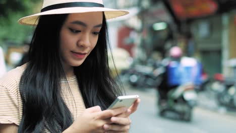 Vista-Portátil-De-Una-Mujer-Vietnamita-Usando-Un-Teléfono-Inteligente-En-La-Ciudad