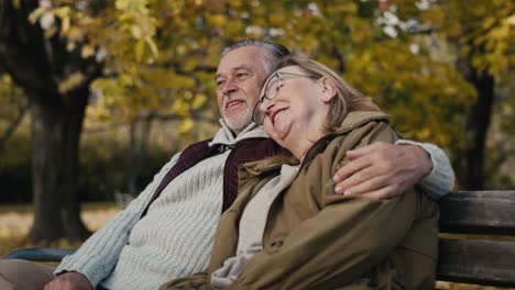 Caucasian-senior-couple-sitting-at-the-bench-at-park-and-embracing