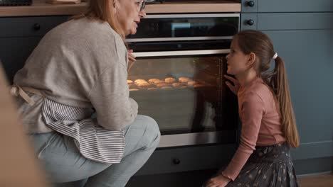 Grandmother-and-granddaughter-waiting-for-homemade-cookies-next-to-the-oven
