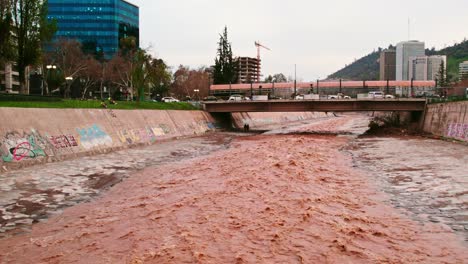 Dolly-in-drone-shot-of-the-flow-of-the-brown-Mapocho-river-and-a-bridge-connecting-the-city-of-Santiago-Chile,-Providencia-sector