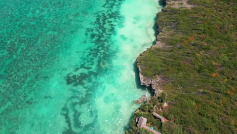 Drone-footage-of-turquoise-sea-resort-by-the-water,-small-bay,-rocky-coast,-green-vegetation,-paradise-like