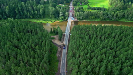Carretera-En-Construcción-Entre-Un-Bosque-Verde-Y-Un-Río-Marrón-Turbio-Desde-Un-Drone-Aéreo-Disparado-En-Letonia