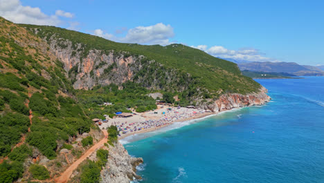 Aerial-drone-forward-moving-shot-over-white-sandy-Gjipe-Beach-with-canyon-in-the-background-in-Albania-on-a-sunny-day