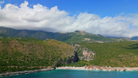 Aerial-drone-backward-moving-shot-over-Gjipe-Beach-and-Canyon-in-Albania-with-white-clouds-passing-in-the-background-on-a-sunny-day