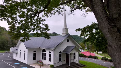 aerial-push-in-to-zionville-baptist-church-with-tree-limbs-in-foreground-in-zionville-nc,-north-carolina-near-boone-nc,-north-carolina