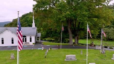 cemetery-with-american-flags-and-baptist-church-in-background-aerial-in-zionville-nc,-north-carolina-near-boone-nc,-north-carolina