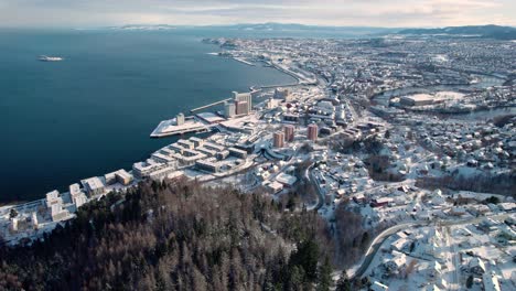 Trondheim-Aerial-Drone-in-winter-covered-with-snow-alongside-river-Nidelva,-Norway