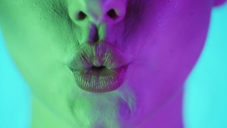 Extreme-Nahaufnahme-Einer-Schönen-Frauenlippe,-Während-Sie-In-Zeitlupe-Einen-Kuss-In-Die-Kamera-Mit-Grün-violettem-Hintergrund-Symbolisiert
