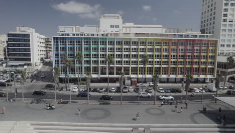 Sliding-drone-shot-in-front-The-colorful-Dan-Hotel-in-Tel-Aviv,-Rainbow-building-on-the-Gordon-promenade-and-Frishman-beach-full-of-visitors-on-a-warm-and-calm-summer-day