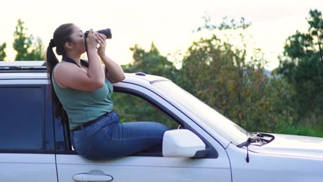 Photographer-woman-sitting-in-the-window-of-her-4x4-offroad-SUV-car-with-a-camera-in-her-hands,-taking-a-photograph