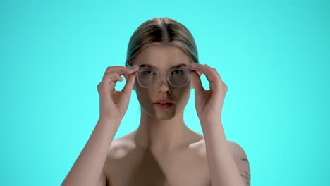 Static-medium-shot-of-a-young-pretty-woman-putting-off-her-glasses-and-looking-into-the-camera-in-front-of-turquoise-background-in-slow-motion