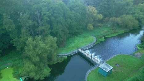 Aerial-Drone-View-Of-A-Person-Standing-Over-River-Culvert-Surrounded-By-Greenery-Dense-Nature-In-Sunrise