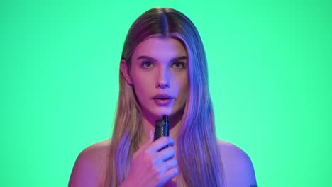 Medium-shot-of-a-young-pretty-woman-taking-a-drag-on-an-electronic-vape-or-electronic-hookah-and-exhaling-the-smoke-in-front-of-green-background-in-slow-motion