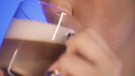 Extreme-close-up-of-a-pretty-woman-while-enjoying-a-freshly-brewed-coffee-latte-macciato-or-cappuccino-in-the-morning-for-breakfast-and-smiling-happily-in-front-of-blue-background-in-slow-motion