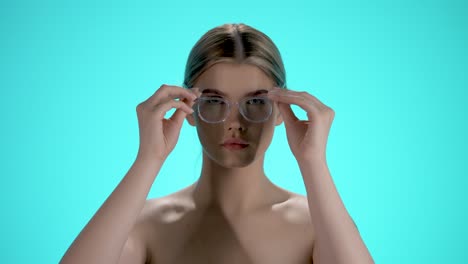 Static-medium-shot-of-a-pretty-young-woman-pulling-her-glasses-on-her-head-and-looking-seductively-into-the-camera-in-front-of-turquoise-background-in-slow-motion