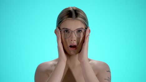 Medium-static-shot-of-a-young-pretty-woman-with-glasses-having-a-frightened-look-and-grabbing-her-head-with-her-hands-in-slow-motion-against-turquoise-background