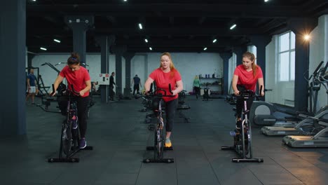 Grupo-De-Mujeres-Atléticas-Viajan-En-Rutina-De-Entrenamiento-De-Bicicleta-Estática-En-El-Gimnasio,-Pérdida-De-Peso-En-Interiores