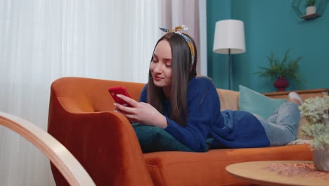 Young-caucasian-woman-lying-on-couch-using-smartphone-watching-video,-online-shopping,-tapping
