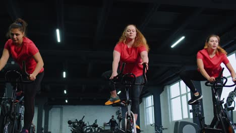 Gesunde-Kaukasische-Gruppe-Von-Frauen,-Die-Im-Fitnessstudio-Auf-Einem-Stationären-Fahrradgerät-Trainieren
