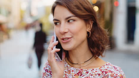 Happy-young-woman-having-remote-conversation-talking-on-smartphone,-good-news-gossip-in-city-street