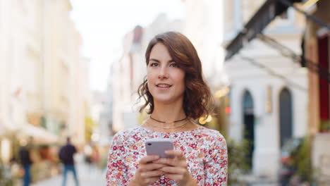 Smiling-woman-girl-using-smartphone-typing-text-answering-messages-chatting-online-in-city-street