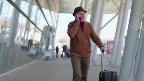 Senior-tourist-grandfather-man-walking-on-international-airport-hall-using-mobile-phone-conversation