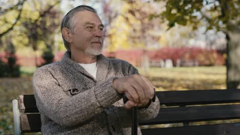 Smiling-old-caucasian-man-sitting-on-bench-in-park-during-the-autumn